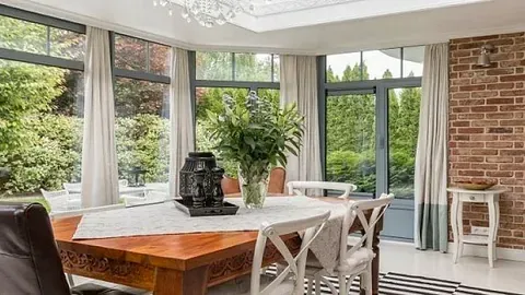 Lyst og moderne spiserom med store vinduer, hvite gardiner og utsikt til grønn hage