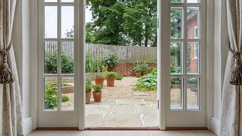 Hvite doble terrassedører med sprosser åpner ut mot en hage med grusgang og grønne planter