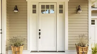 Hvit ytterdør med små vinduer øverst, omgitt av beige kledning og to blomsterkrukker