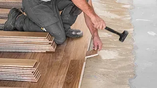 Håndverker legger parkettgulv med lim, iført arbeidsklær og bruker gummihammer